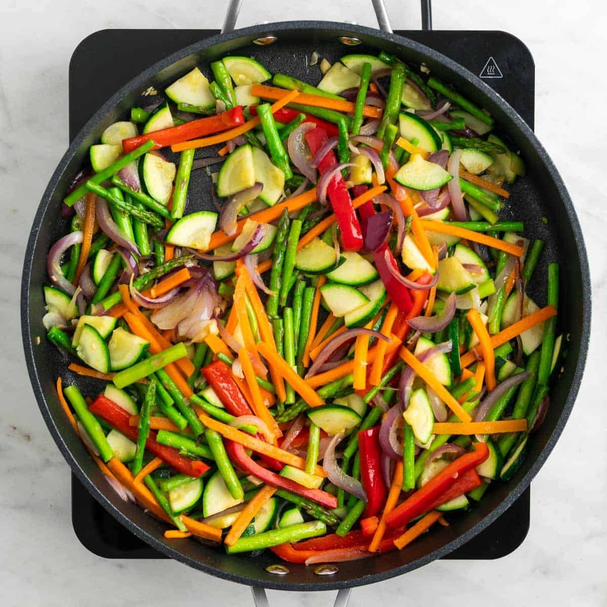 Asparagus, carrot, zucchini, and red bell pepper cooking in a skillet