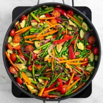 Peas, cherry tomatoes, and seasonings added to the vegetables in a skillet