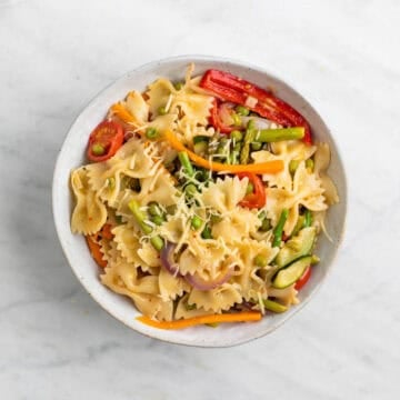 Vegan pasta primavera topped with fresh basil and vegan cheese on a plate