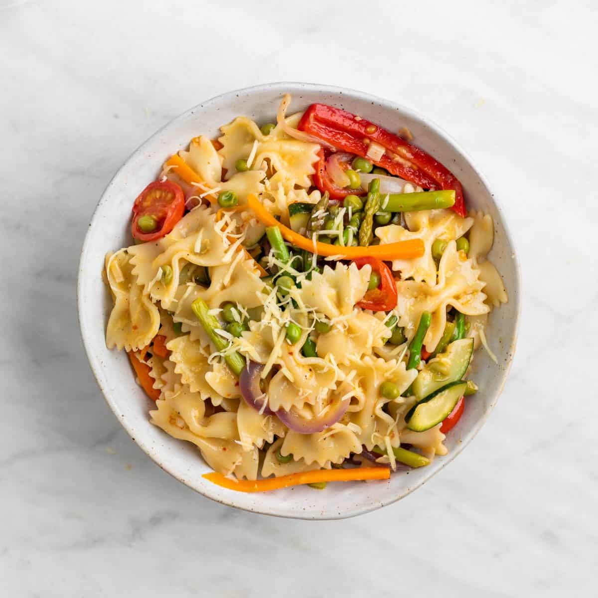 Vegan pasta primavera topped with fresh basil and vegan cheese on a plate