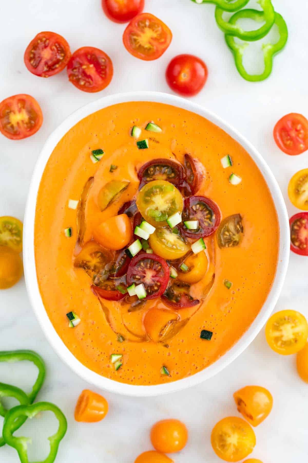 Bowl of gazpacho garnished with sliced cherry tomatoes, cucumber, and olive oil