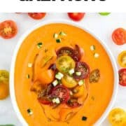 Smooth gazpacho in a bowl topped with cucumber, cherry tomatoes, and olive oil
