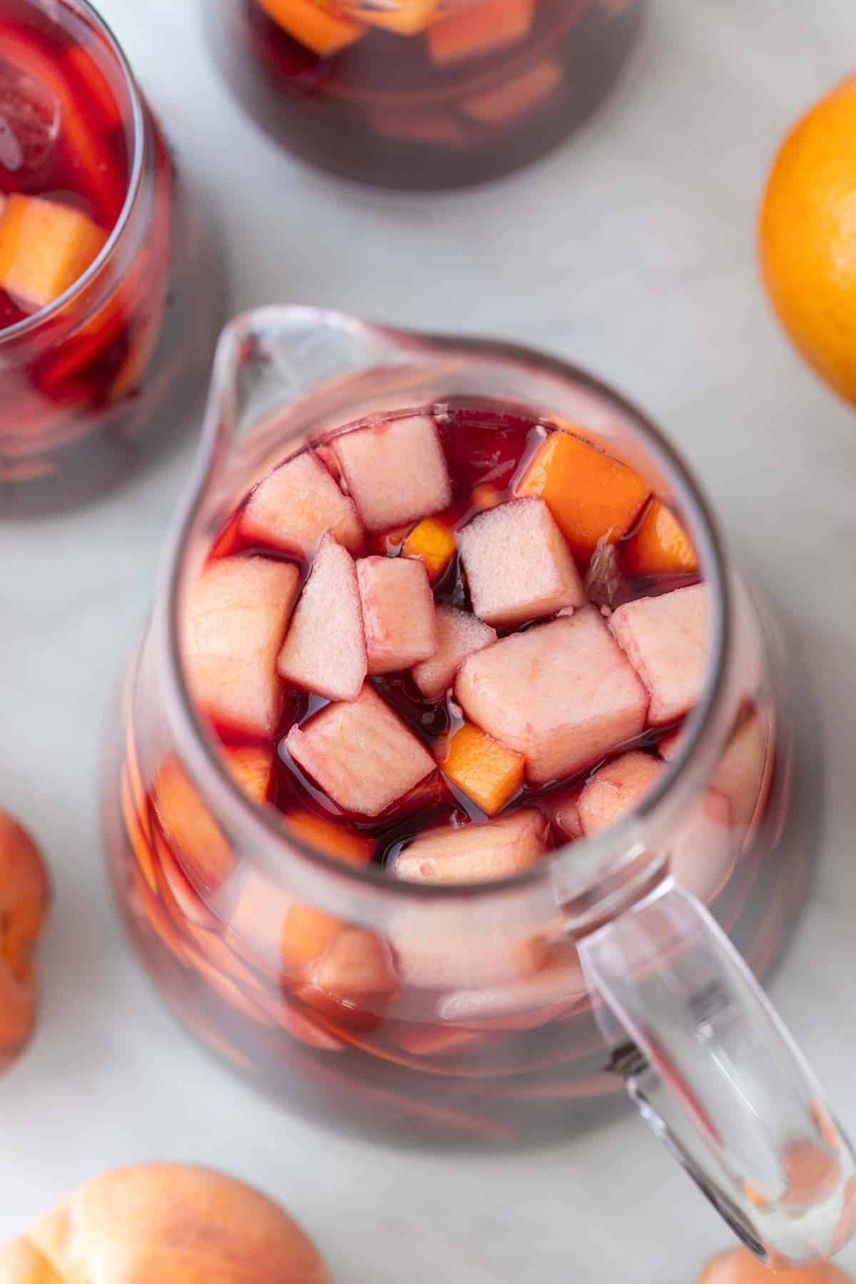 Pitcher and two glasses of Spanish sangria with fresh fruit around them