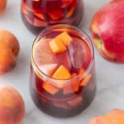 Two glasses of homemade sangria with ice and fresh fruit arranged around them