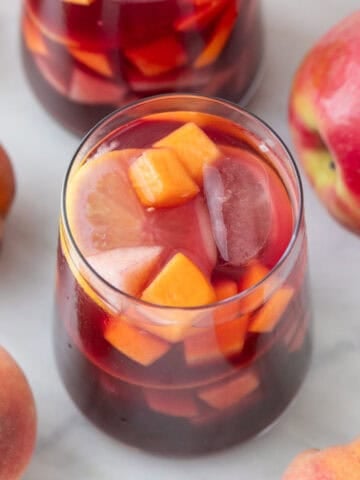 Two glasses of homemade sangria with ice and fresh fruit arranged around them