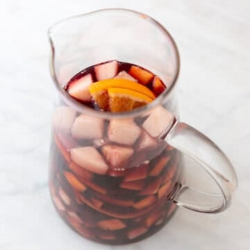 Chopped fruit, red wine, simple syrup, and orange juice in a pitcher