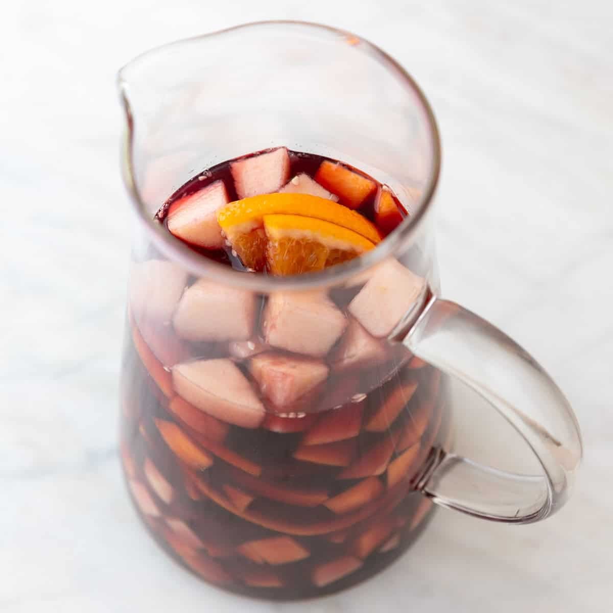 Chopped fruit, red wine, simple syrup, and orange juice in a pitcher