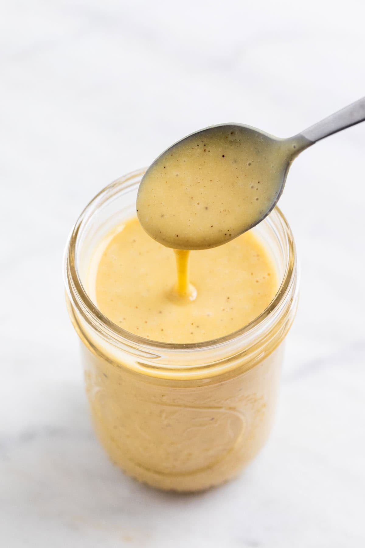 Spoon pouring creamy vegan salad dressing into a glass jar