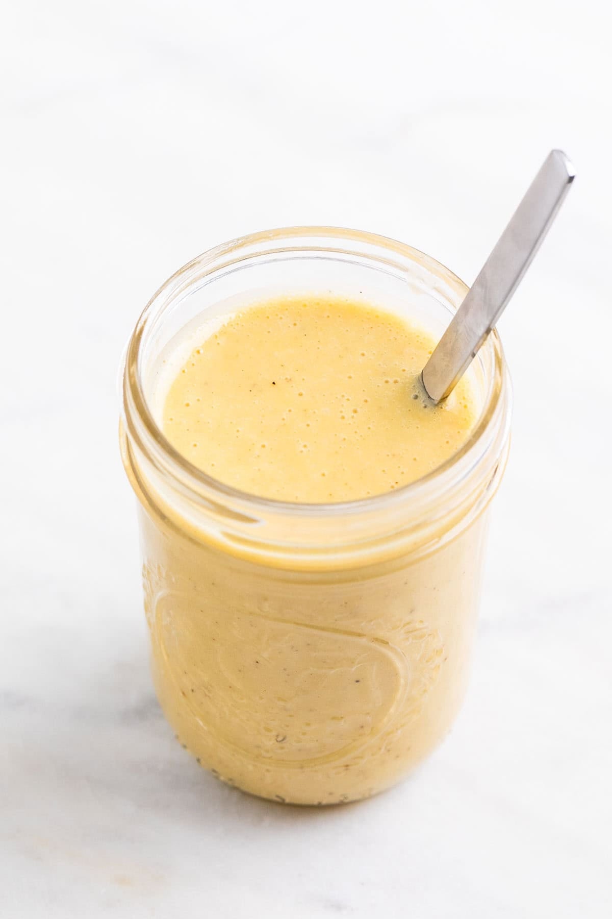 Vegan salad dressing in a glass jar with a spoon inside