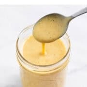 Vegan salad dressing being poured into a jar with a spoon