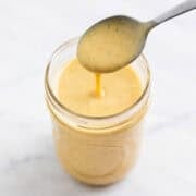 Creamy vegan salad dressing dripping from a spoon into a glass jar