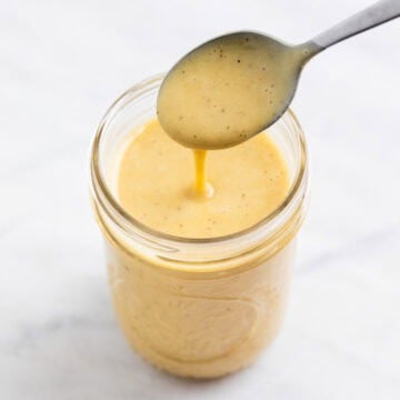 Creamy vegan salad dressing dripping from a spoon into a glass jar