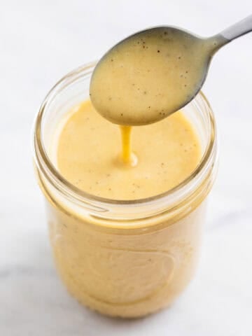 Creamy vegan salad dressing dripping from a spoon into a glass jar