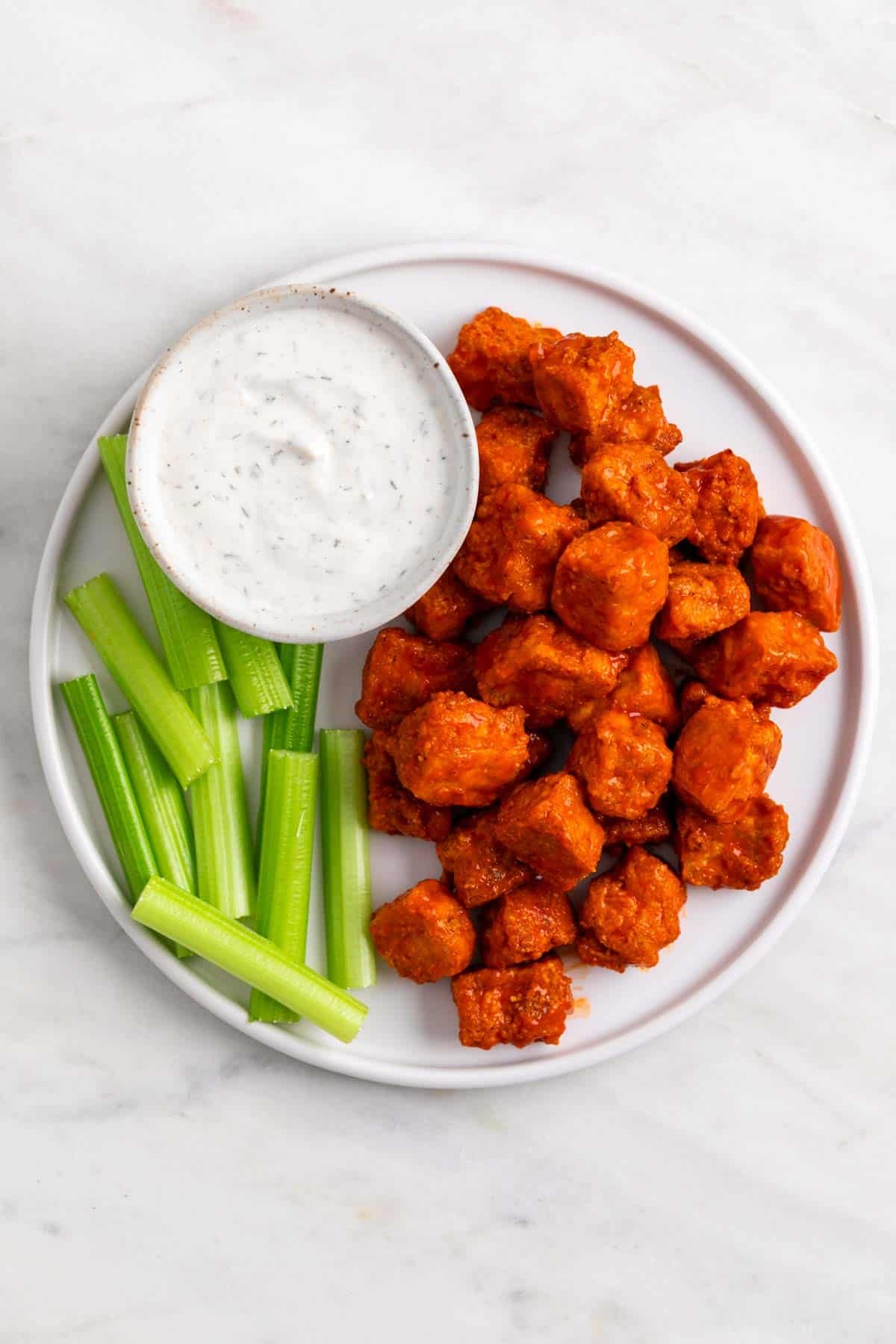 Buffalo tofu on a plate with celery sticks and vegan ranch dressing