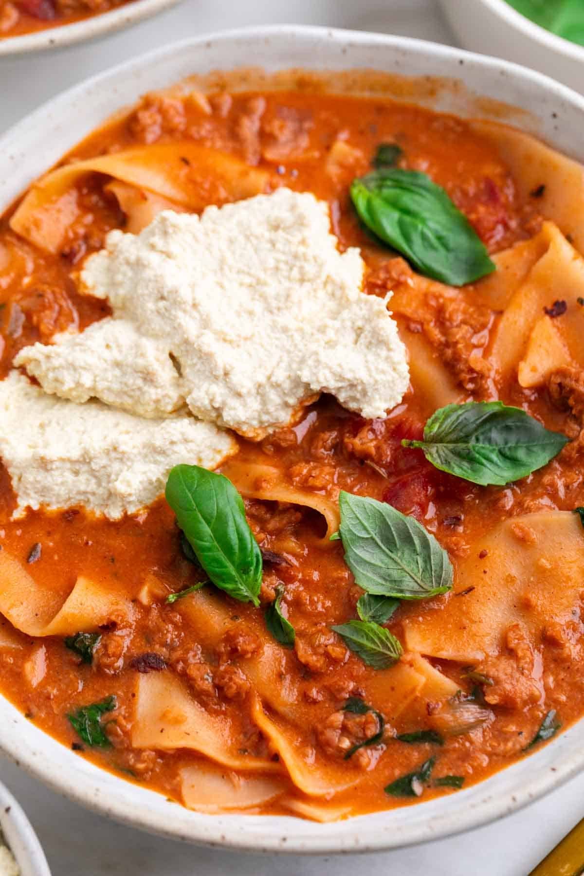 Bowl of lasagna soup topped with vegan ricotta and fresh basil