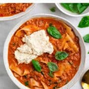 Two bowls of vegan lasagna soup with ricotta, basil, and ingredients on the side