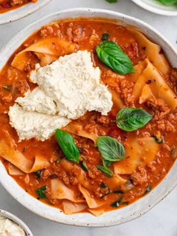 Vegan lasagna soup in a bowl with vegan ricotta and basil on top