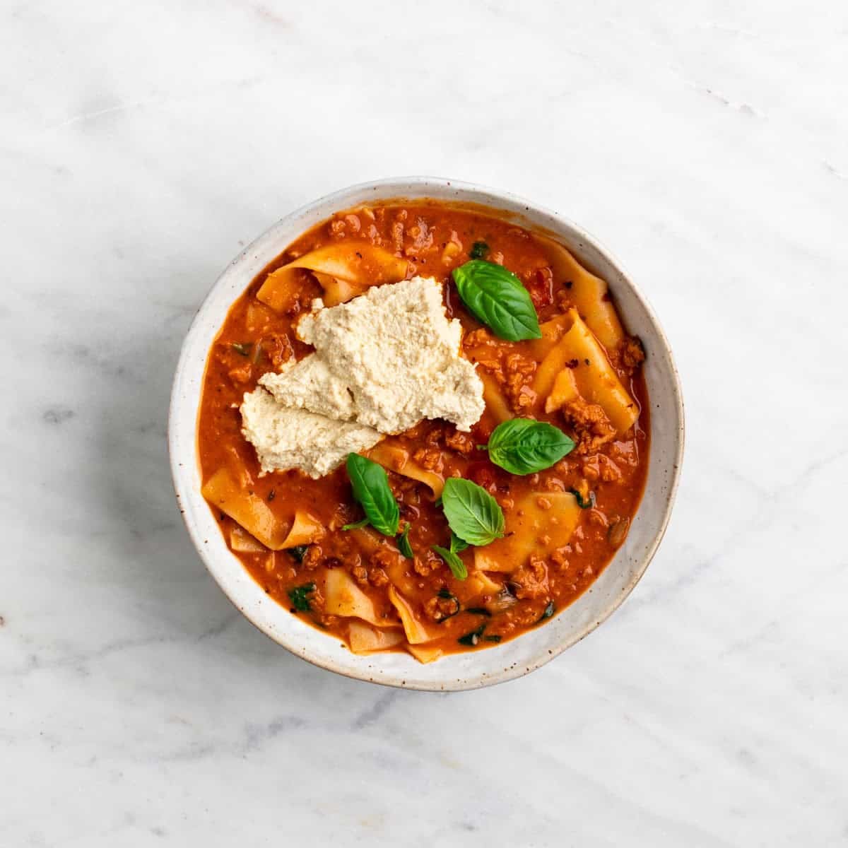 Lasagna soup served in a bowl with vegan ricotta and basil