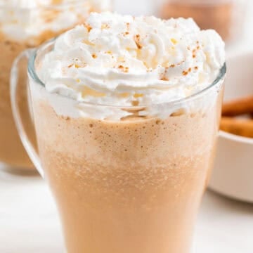 Two mugs filled with vegan pumpkin spice latte, vegan whipped cream, and pumpkin pie spice