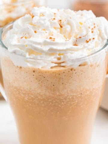 Two mugs filled with vegan pumpkin spice latte, vegan whipped cream, and pumpkin pie spice