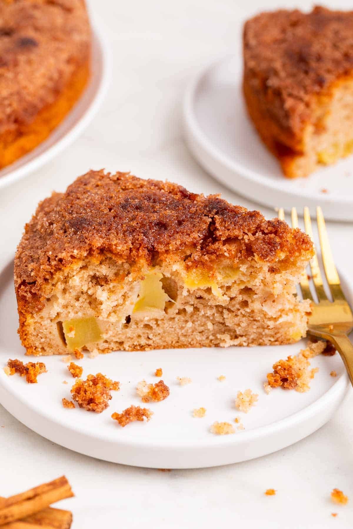 Slice of apple cake with cinnamon sugar topping and the rest of the cake behind