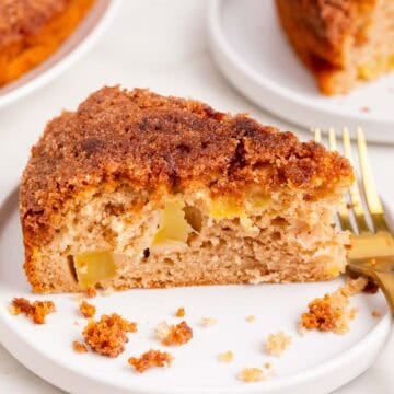 Slice of vegan apple cake on a plate with fork and whole cake behind