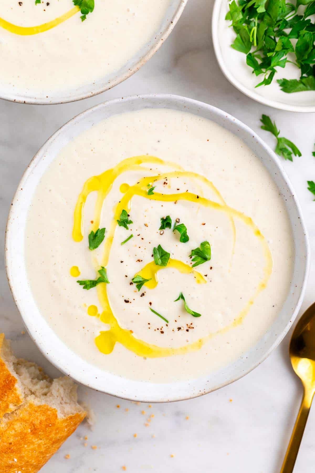 Two bowls of vegan cauliflower soup with olive oil, black pepper, and parsley