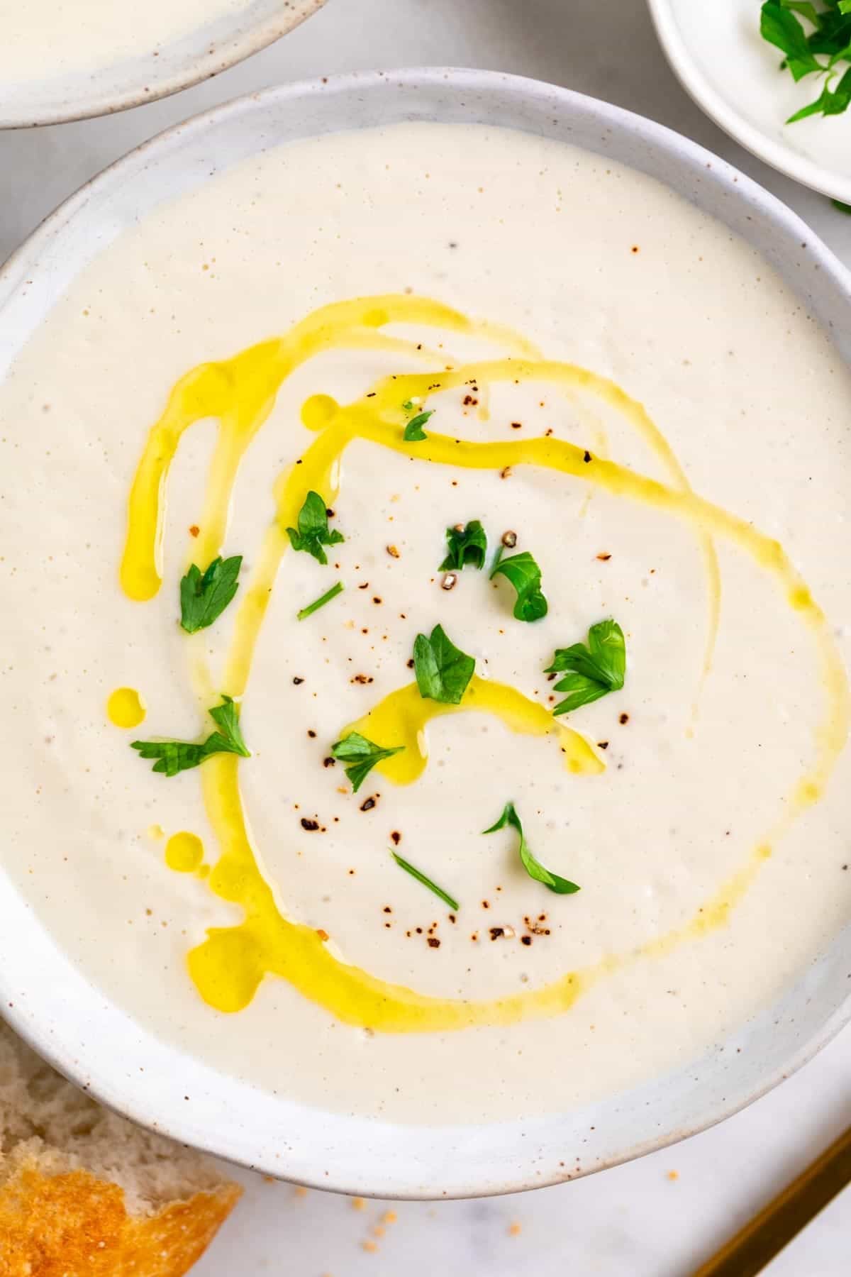 Creamy vegan cauliflower soup served with bread, a spoon, and fresh parsley