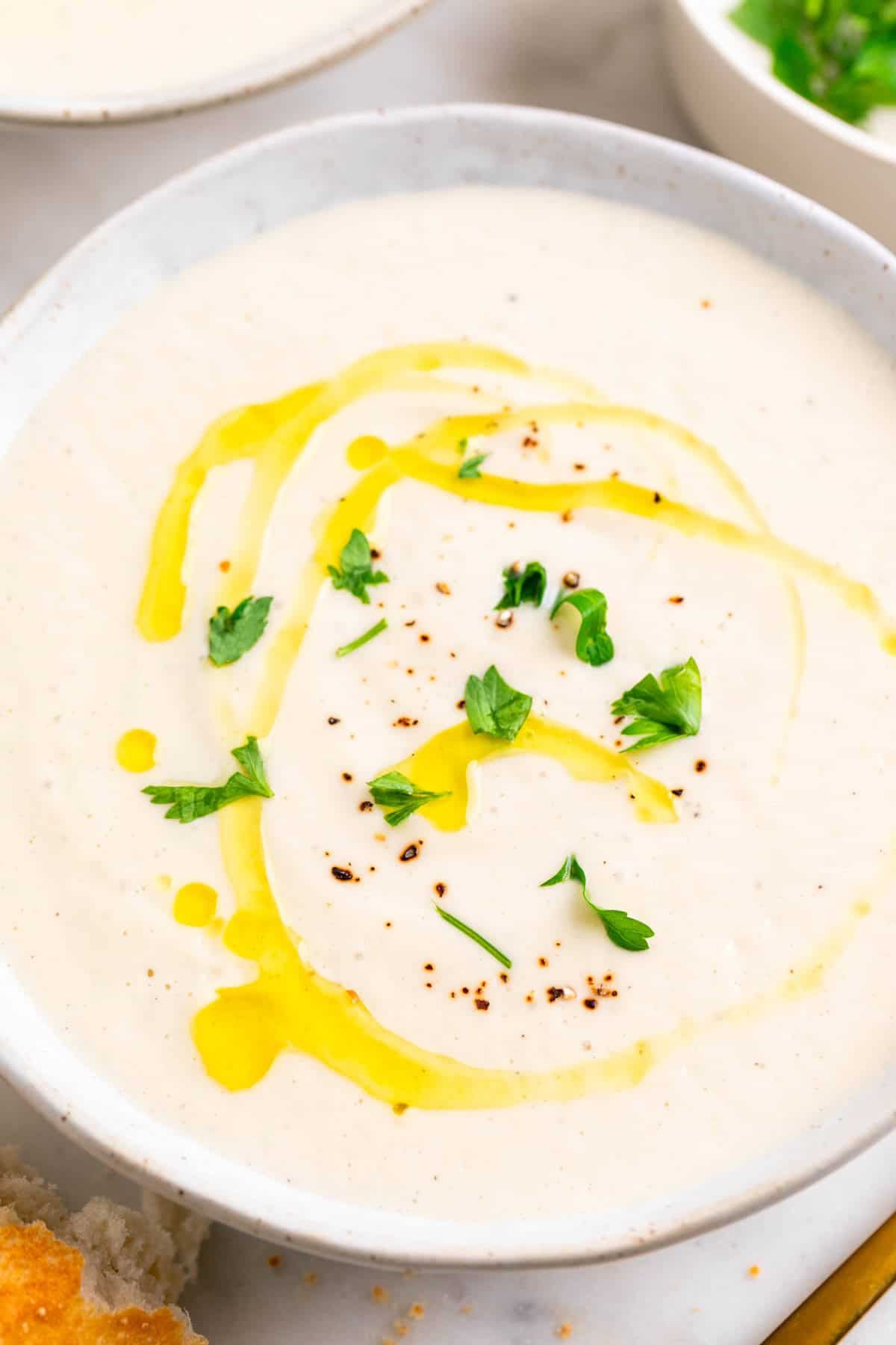 Two bowls of cauliflower soup topped with olive oil, black pepper, and parsley