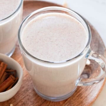 Vegan eggnog in two glass jars on a wooden board with cinnamon sticks and chopped cashews