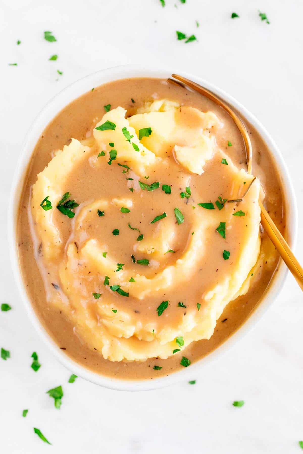 Vegan mashed potatoes topped with gravy and chopped parsley in a bowl with a fork