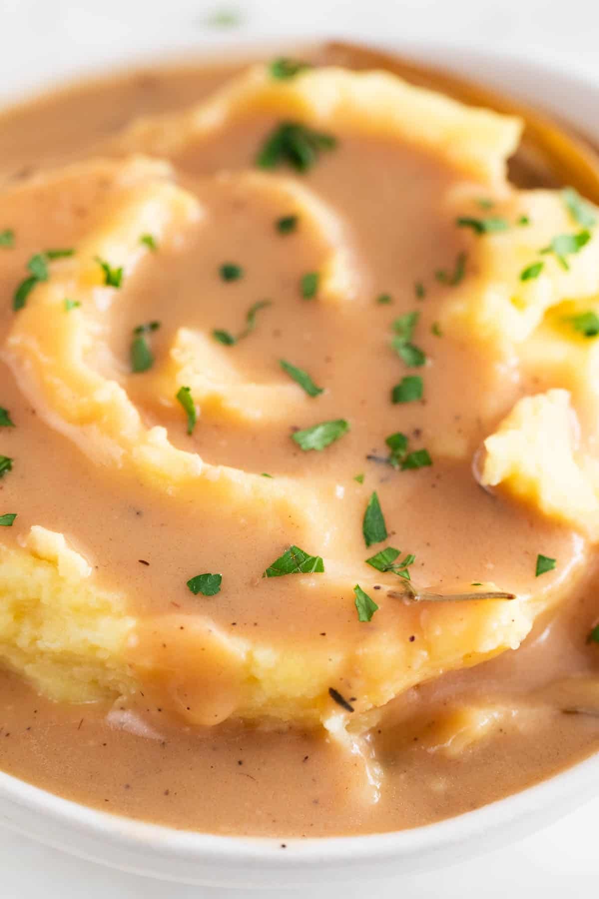 Creamy vegan gravy served over mashed potatoes with fresh parsley and a fork
