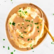 Vegan mashed potatoes with rich, creamy gravy, chopped parsley, and a fork in the bowl