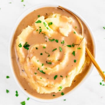 Vegan mashed potatoes with rich, creamy gravy, chopped parsley, and a fork in the bowl