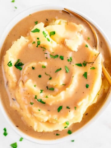 Vegan mashed potatoes with rich, creamy gravy, chopped parsley, and a fork in the bowl