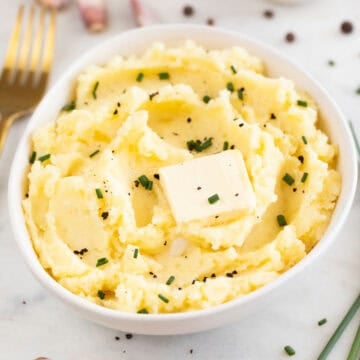 Bowl of vegan mashed potatoes with butter, chives, and black pepper, with a fork