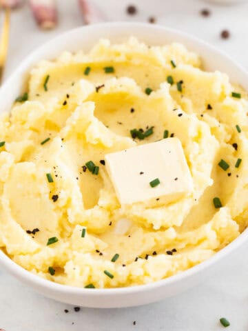 Bowl of vegan mashed potatoes with butter, chives, and black pepper, with a fork