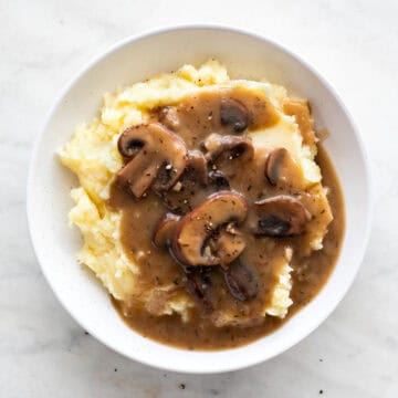 Bowl of vegan mashed potatoes smothered in mushroom gravy and topped with black pepper